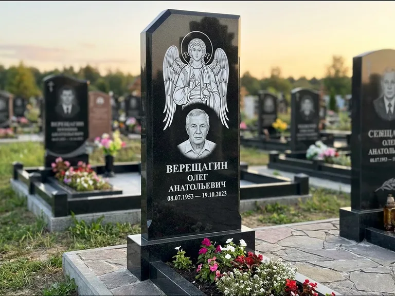 Памятник с гравировкой иконы: стела с резным навершием и нимбом в золоте — гравировка образа Спасителя, высокие разросшиеся туи полукругом, работа «Мельникова» в Уфе