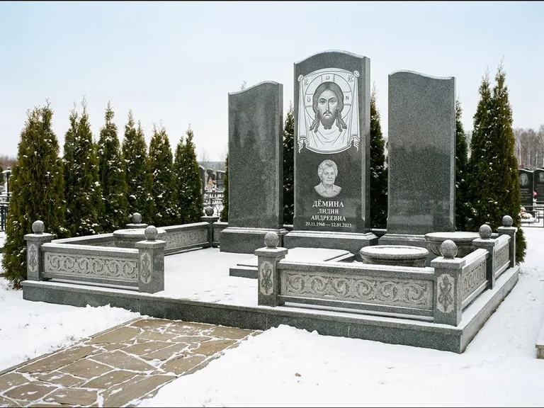 Памятник с гравировкой иконы: узкая вертикальная стела-пилон с ликом — икона в резной рамке-киоте, открытая лужайка без ограды, работа «Одинцов» в Уфе